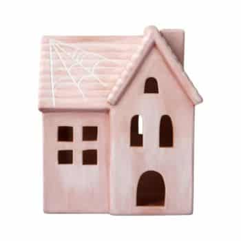 A small, pink ceramic house with a simple design featuring square and arched windows. The roof has a white cobweb pattern, giving it a charming, slightly spooky appearance.