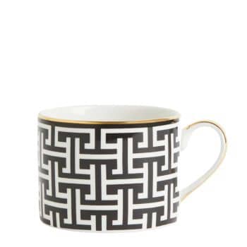 A white ceramic mug with a black geometric pattern and a gold rim around the top edge. The handle of the mug is small and also accented with gold. The design is modern and intricate, giving the mug an elegant appearance.