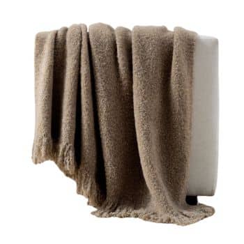 A soft, brown, textured blanket draped over the arm of a light-colored sofa. The blanket has a slightly fluffy appearance and hangs down casually, creating a cozy and inviting look.