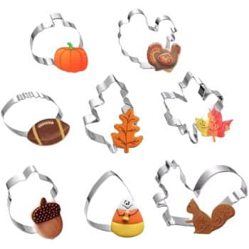 A collection of nine metal cookie cutters in various autumn-themed shapes, including a pumpkin, turkey, football, leaf, and acorn. Each cookie cutter is paired with an autumn cookie that matches its shape, showcasing colorful fall designs.