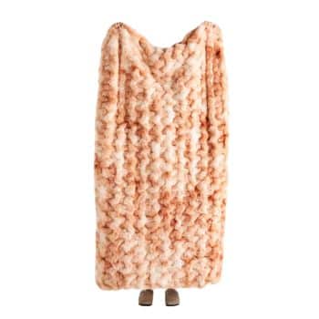 A person stands wrapped in a large, textured, peach-colored blanket that covers their entire body except for their feet, which are visible at the bottom.