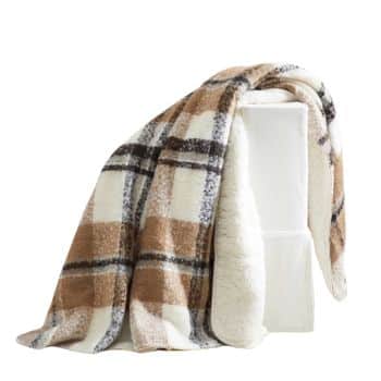 A soft, cozy blanket with a brown, black, and white plaid pattern is draped over a white cube-shaped object. The blanket appears warm and inviting, suitable for use in cold weather.