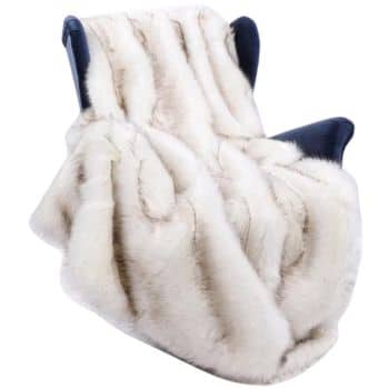 A luxurious cream-colored faux fur throw blanket is draped over a dark blue armchair. The blanket appears soft and plush, creating a cozy and elegant atmosphere.