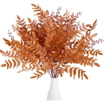 A white vase holds a vibrant arrangement of dried orange ferns and eucalyptus branches, with a few berries interspersed. Perfect for fall decor ideas, the foliage creates a full, fan-like display that spreads outward from the vase.