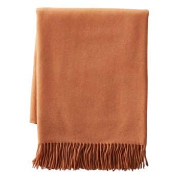 A neatly folded, solid-colored rust-orange blanket with a fringe border at the bottom. The fabric appears soft and warm, suitable for cozying up or for use as a decorative throw on furniture.