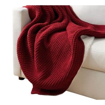 A cozy red knit blanket is draped over the arm of a white sofa, creating an inviting and warm atmosphere.