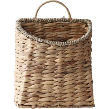 A rectangular, woven wicker basket with a sturdy, curved handle on top. The basket has a natural, light brown color with variations in the weave pattern, giving it a rustic appearance. Perfect for fall decor ideas, the open top of the basket slightly tapers wider than the base.