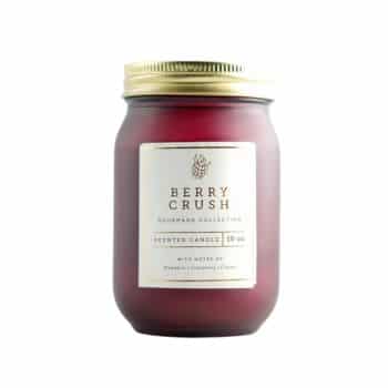 A red jar candle with a gold lid labeled "Berry Crush" from the Gourmet Collection. The label mentions scents of raspberry, cranberry, and cherry.