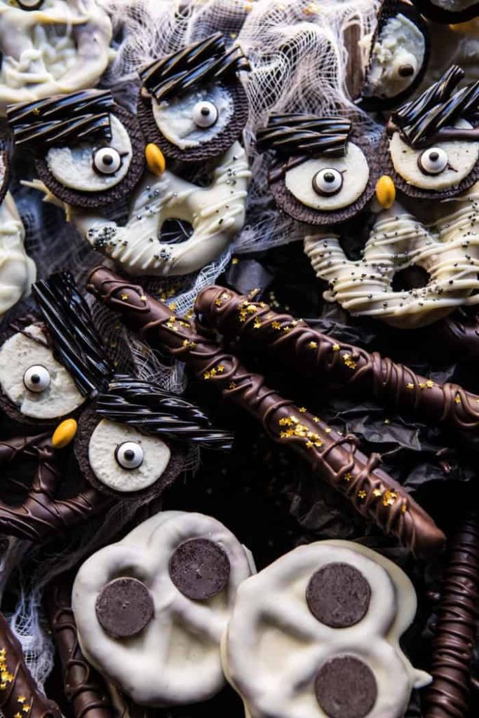 A festive collection of Halloween treats for kids featuring chocolate-covered pretzels with candy eyes and sprinkles, and cookies shaped like owls with licorice feathers and candy eyes, all set against a spooky backdrop.