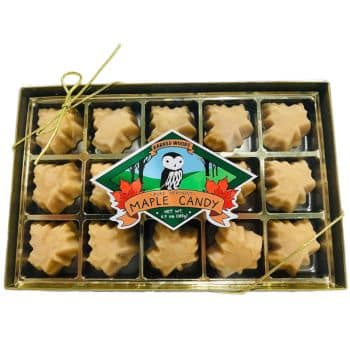 A box of maple leaf-shaped candies arranged in a 4x4 grid, secured with a gold ribbon. The packaging features a label with an owl illustration, reading "Maple Candy." Each candy is a light brown color, typical of maple confections.