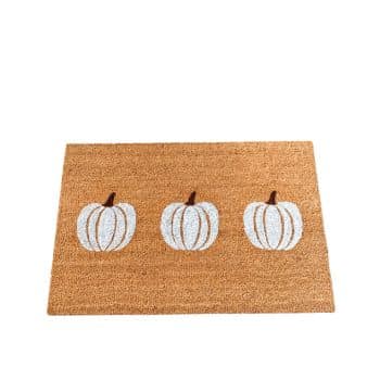 A doormat with a natural coir texture featuring three white pumpkins arranged in a row. The background is plain, highlighting the autumnal theme.