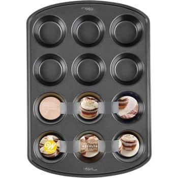 A 12-cup nonstick muffin pan with a black finish is perfect for crafting your favorite fall dessert recipes. Three of the cups display cardboard inserts showing images of cupcakes and product details.