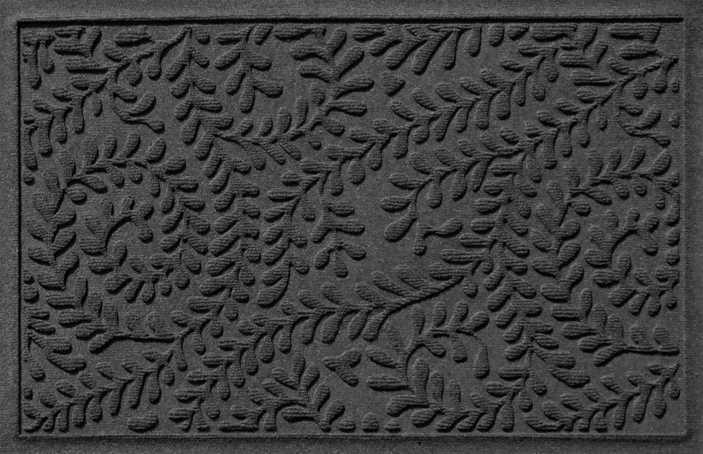 A rectangular doormat with an intricate embossed pattern of swirling leaf designs on a textured surface. Perfect for fall decorating ideas, the design features overlapping vines and leaves, giving it an elegant and decorative appearance. The mat is in a dark gray color.