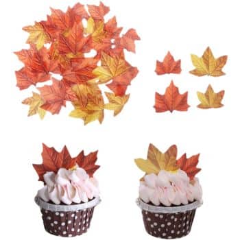 Cupcakes with pink frosting in polka dot wrappers are topped with orange and yellow autumn leaf decorations, perfect for any fall dessert recipe. Additional leaf decorations are shown separately in small groups.