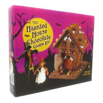 The image displays a Trader Joe's Haunted House Chocolate Cookie Kit, perfect as Halloween treats for kids. The spooky-themed packaging showcases a chocolate cookie house adorned with icing and candy, set against silhouettes of a witch and bats in a moonlit sky.