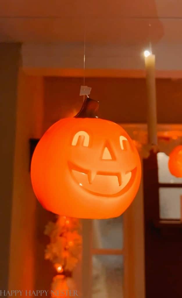 A glowing, orange jack-o'-lantern with a carved smiling face, created through easy pumpkin crafts, hangs from the ceiling, illuminating a cozy, dim room.