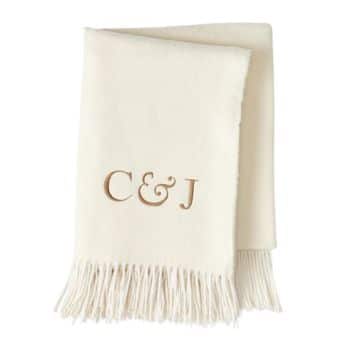 A cream-colored blanket with tasseled edges features the initials "C & J" embroidered in brown.