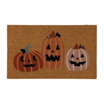 A rectangular doormat featuring three cartoon carved pumpkins with smiling faces. The pumpkins are placed side by side, each with a unique design. The background is a natural coir material, and the overall theme is festive and Halloween-related.