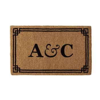 A rectangular brown doormat with black decorative corner designs and the letters "A & C" in bold black print at the center.