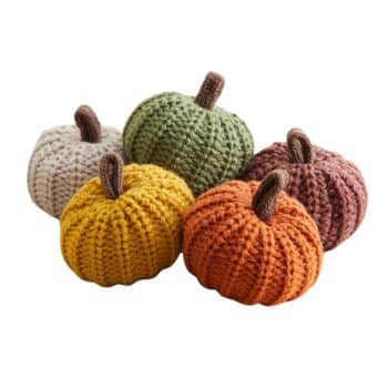 A group of five crocheted pumpkins in different colors—cream, yellow, green, orange, and rust—offers easy pumpkin crafts for autumn. Each boasts a short brown stem, arranged on a plain background to showcase a cozy seasonal theme.