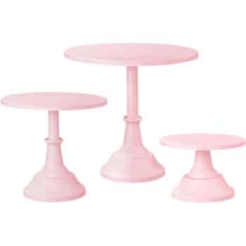 Three pastel pink cake stands of varying heights are arranged in a group, perfect for showcasing fall pies and cakes. Each stand features a round top and a wide, tapered base, adding elegance to any dessert display.