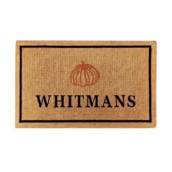 Rectangular doormat with a beige color and a black border. The word “WHITMANS” is centered in bold black letters, and above it is an orange pumpkin outline.