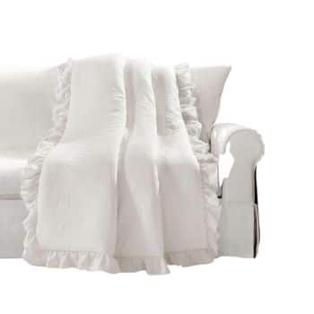 A white ruffled blanket draped over the arm of a white sofa. The blanket has a textured pattern and adds a touch of elegance to the minimalist furniture.