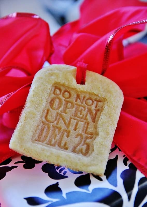 A close-up of a rectangular cookie, hailed as one of the best Christmas cookies, embossed with "Do Not Open Until Dec 25." It's tied with a red ribbon atop a black-and-white patterned surface.