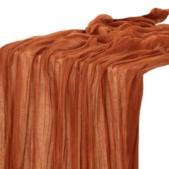 A draped piece of sheer, lightweight fabric in a warm terracotta color, with soft folds and a textured appearance. The cloth appears smooth and slightly transparent, showcasing elegant and flowing lines.