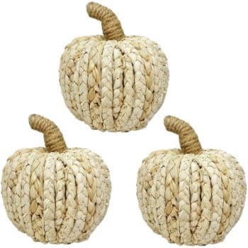 Three decorative pumpkins made from woven straw are arranged against a plain white background. Each pumpkin has a textured surface and a short, twisted stem, giving them a rustic, natural appearance.