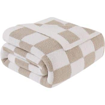 A folded blanket with a checkered pattern in beige and white. The texture appears soft and plush, suggesting warmth and comfort.