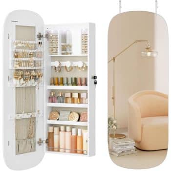 A mirrored jewelry cabinet is open, revealing neatly organized accessories and cosmetics. The left side displays earrings and necklaces, while the right side has shelves with skincare products. The mirror reflects a soft pink chair and a floor lamp.