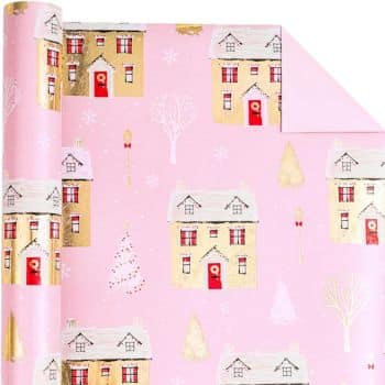 A roll of pink wrapping paper featuring illustrations of houses with red doors, snow-covered roofs, and trees. The design has a festive holiday theme with subtle hints of gold.