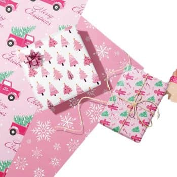 Pink and white Christmas-themed gift wrap with illustrations of trees, snowflakes, and a vintage truck. Two wrapped gifts are adorned with decorative bows and twine on a pink backdrop.