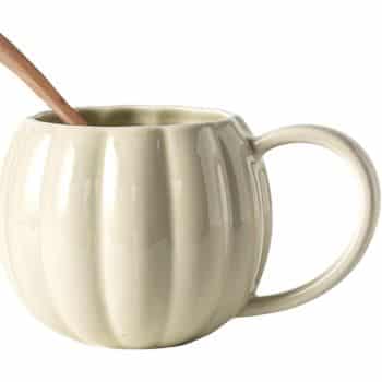 A cream-colored, pumpkin-shaped ceramic mug with a large handle, holding a wooden spoon inside.