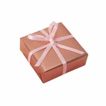 A square gift box wrapped in shiny rose gold paper and tied with a light pink ribbon in a bow.