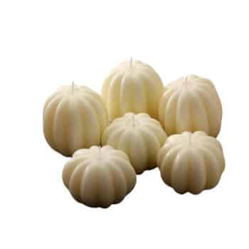 A group of six cream-colored candles shaped like pumpkins, arranged in a cluster. The candles vary in size, creating a visually appealing display. The background is plain white, highlighting the candles' unique shape.