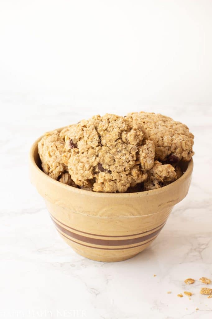 A brown striped ceramic bowl filled with the best Christmas cookies, featuring chunky oatmeal delights, sits on a white marble surface. Cookie crumbs are scattered around the bowl, adding a rustic touch to the festive scene.