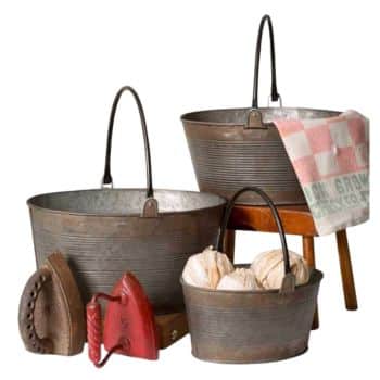 Vintage household items including two old metal buckets with handles, fabric balls, two antique irons, and a red-checked cloth on a wooden stool.