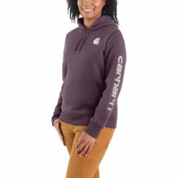 A person wearing a purple Carhartt hoodie with the logo on the sleeve and chest, paired with tan pants. They are standing and smiling.