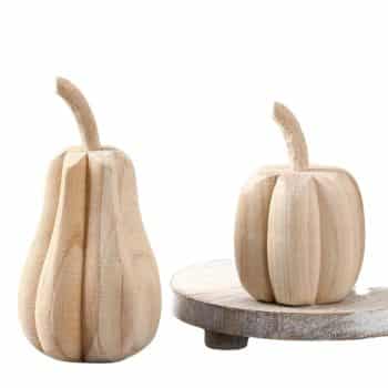 Two carved wooden sculptures resembling a pear and a pumpkin are displayed on a wooden surface. The smooth, light wood texture adds a rustic charm to the scene.