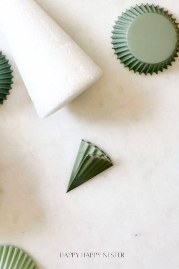 DIY craft materials on a white surface, including green paper circles and a styrofoam cone.