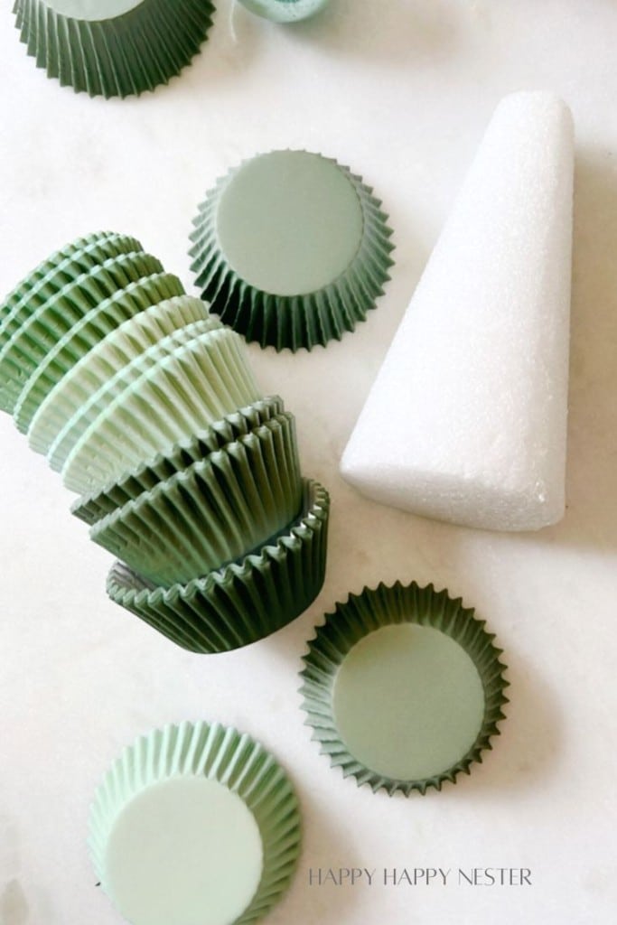 A stack of green cupcake liners and several single liners are arranged on a white surface next to a white foam cone.