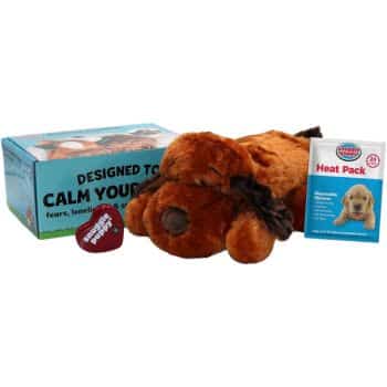 A plush dog toy with a heartbeat feature, accompanied by a heat pack and packaging that reads "Designed to calm your pet's fears, loneliness, and anxiety." The set includes a small red heart shape labeled "Real-feel Heartbeat.