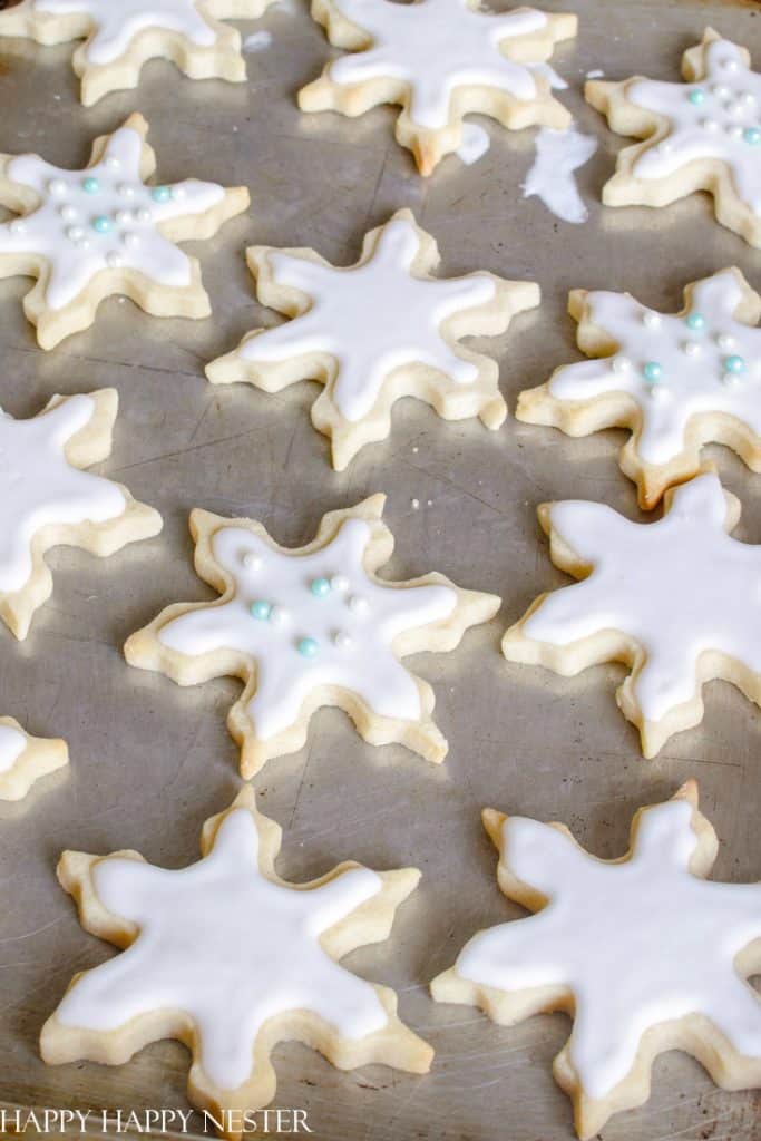 Snowflake-shaped sugar cookies with white icing, hailed as some of the best Christmas cookies, are arranged on a baking sheet. Some are adorned with small blue and white sugar pearls.