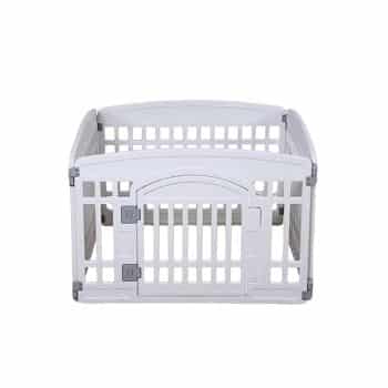 A white plastic playpen with a front gate, featuring vertical slats and rounded top edges. The playpen is empty and set against a plain white background.