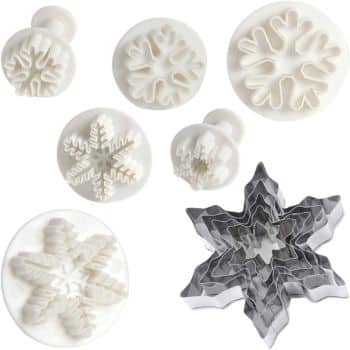 A variety of snowflake-shaped cookie cutters are displayed, perfect for crafting the best Christmas cookies. The set includes white plastic cutters with embossed designs and metallic silver cutters, each featuring unique snowflake patterns.