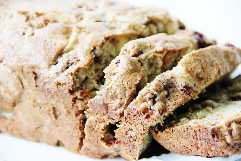 Close-up of sliced banana bread with walnuts on a white plate. This delightful Christmas treat is golden brown with visible chunks of nuts and banana, showcasing its moist, fluffy texture.