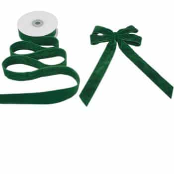 A roll of green velvet ribbon next to a matching green velvet bow.