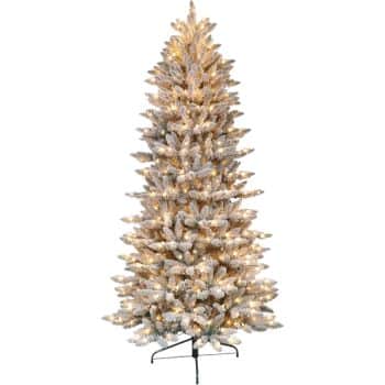 A tall, artificial Christmas tree with frosted, white branches and glowing yellow lights, standing on a metal base.